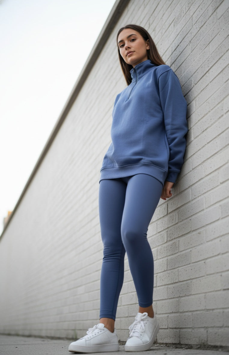 Woman in blue athletic outfit leaning against a white brick wall.